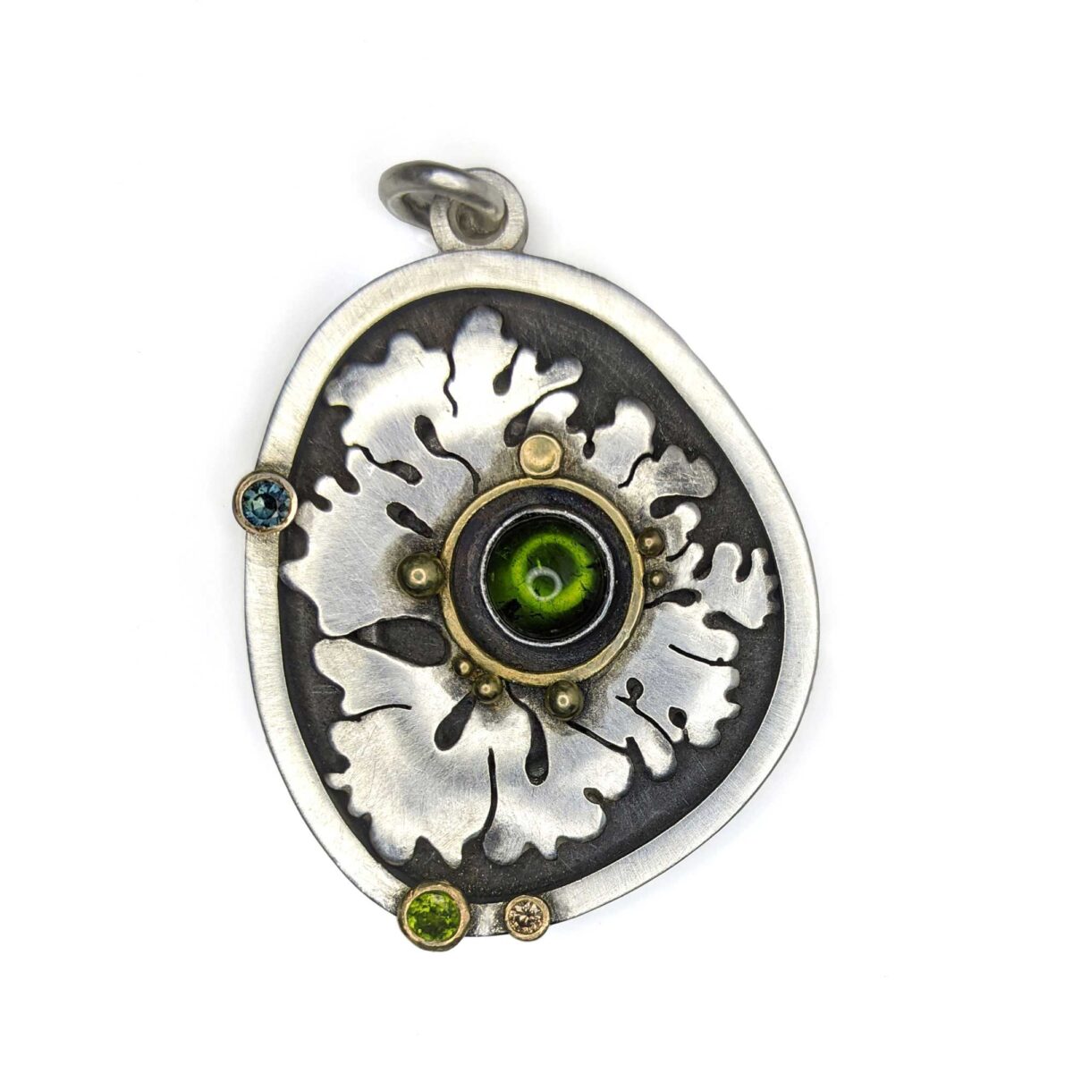 A silver pendant with a floral/leaf motif studded with green and blue stones.