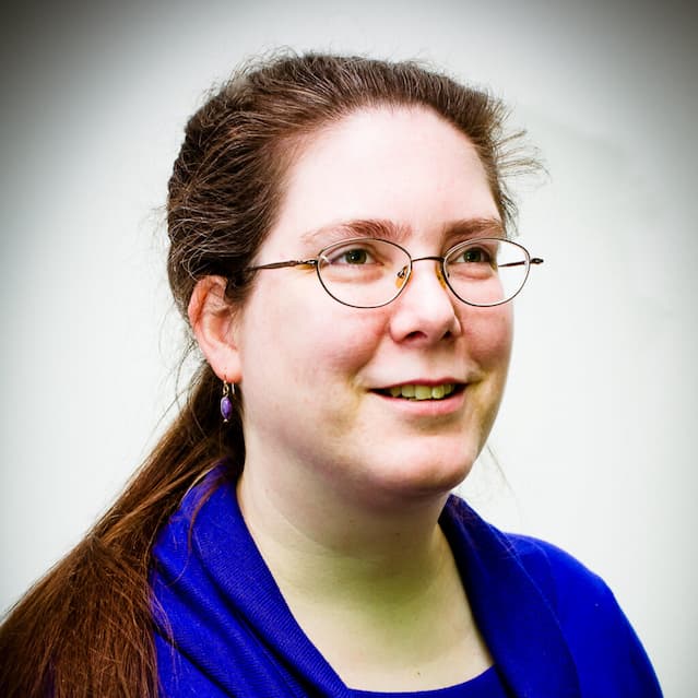 A photograph of Genevieve Cogman, a white woman with dark hair, looking to the right of the frame.