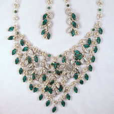 Photograph of a silver necklace with green and white droplet shaped stones. In the middle, several of the white stones are arranged to make flower shapes.